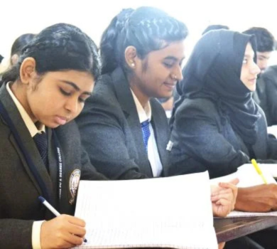 Close up of female students in grey blazers and ties writing in their notebooks during a lecture.