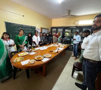 A group of students and teachers gathered in a staff room, displaying prepared dishes on a long table.
