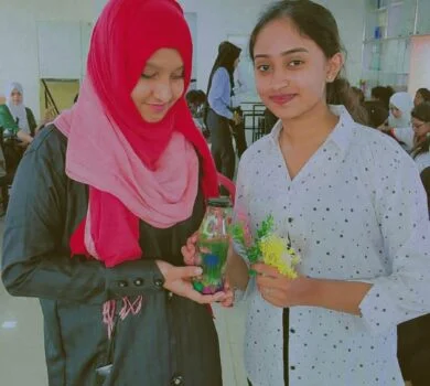 Two smiling students presenting a crafted item in a jar.
