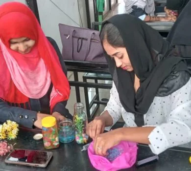 Students sitting at a desk, carefully crafting decorative items inside glass jars.