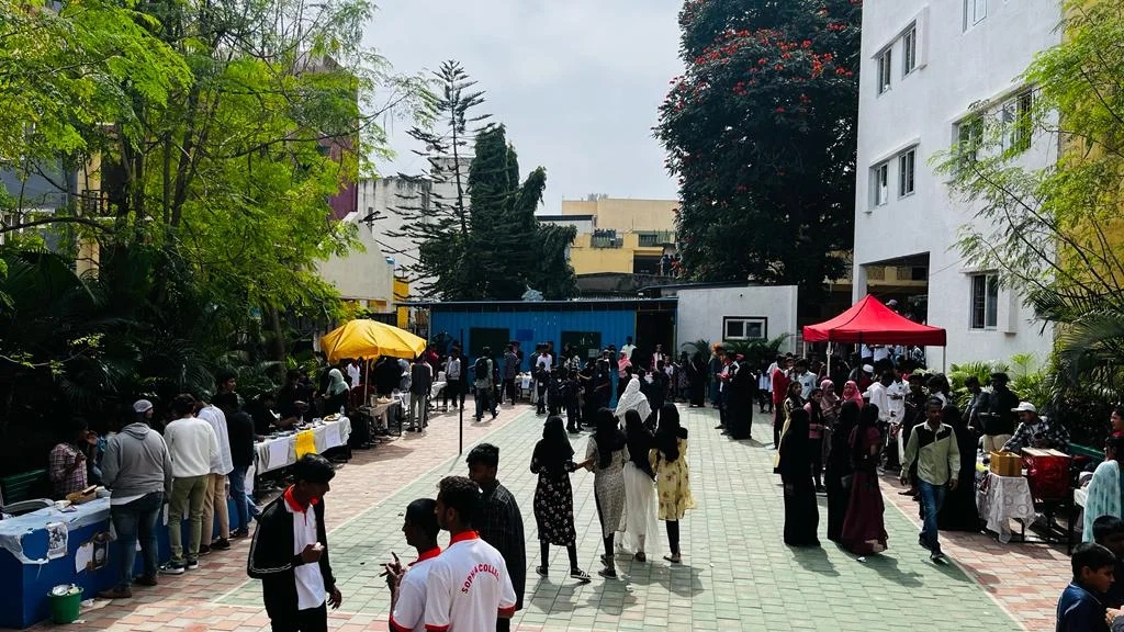 A busy college courtyard with students, food stalls, and a red tent.