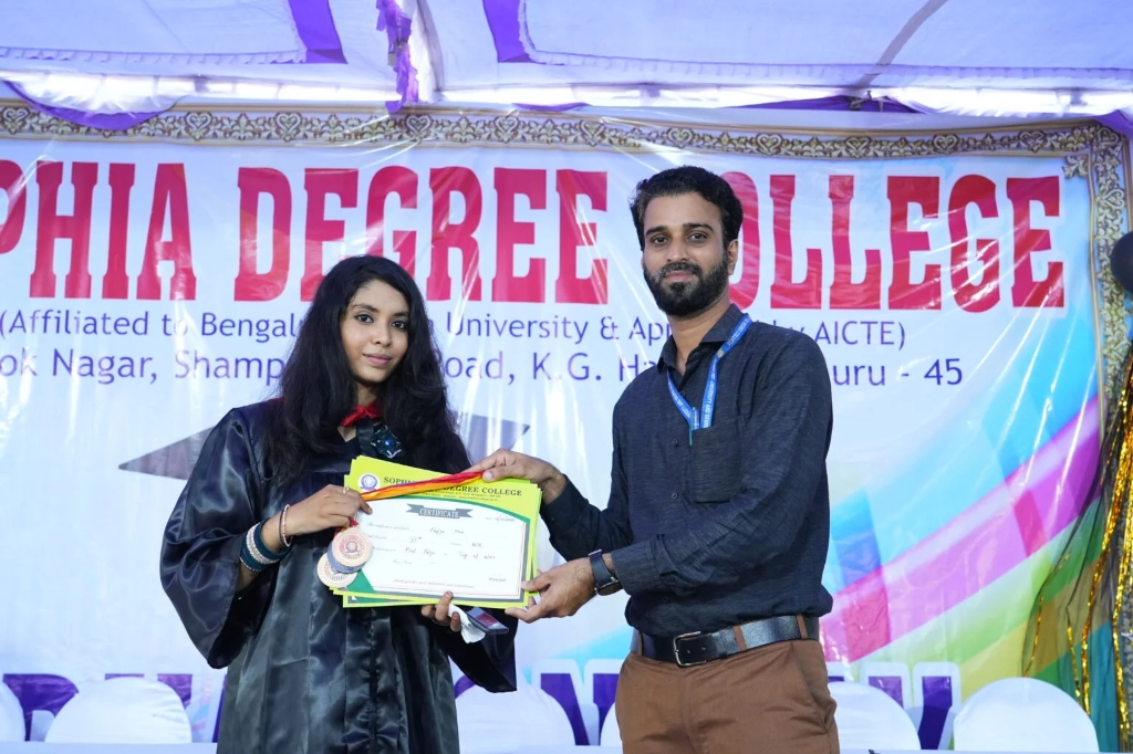 A female graduate in a graduation gown receiving a certificate and medal.