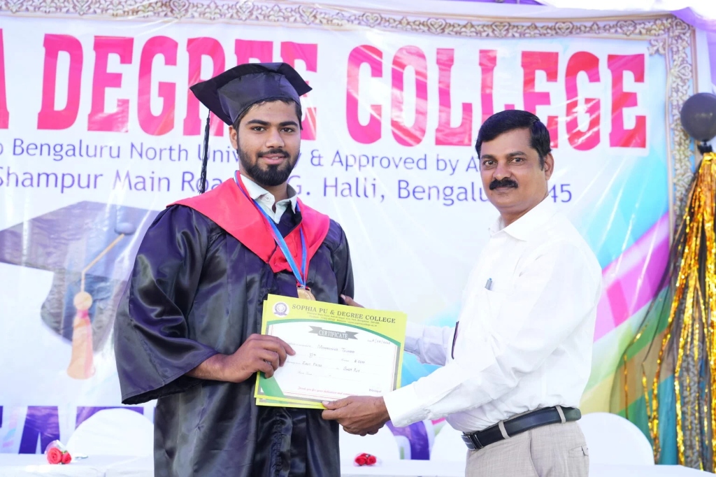 A male graduating student in a gown receiving his certificate.