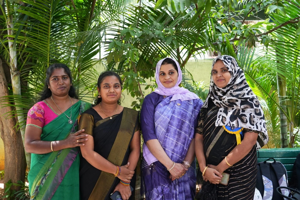 Four female faculty members smiling for a picture at the graduation ceremony.