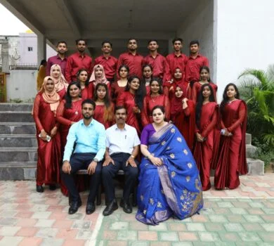 Students in maroon sarees and shirts taking a group photograph with faculty.