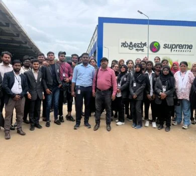 A large group photo of students and faculty outside the Supreme Products factory building.