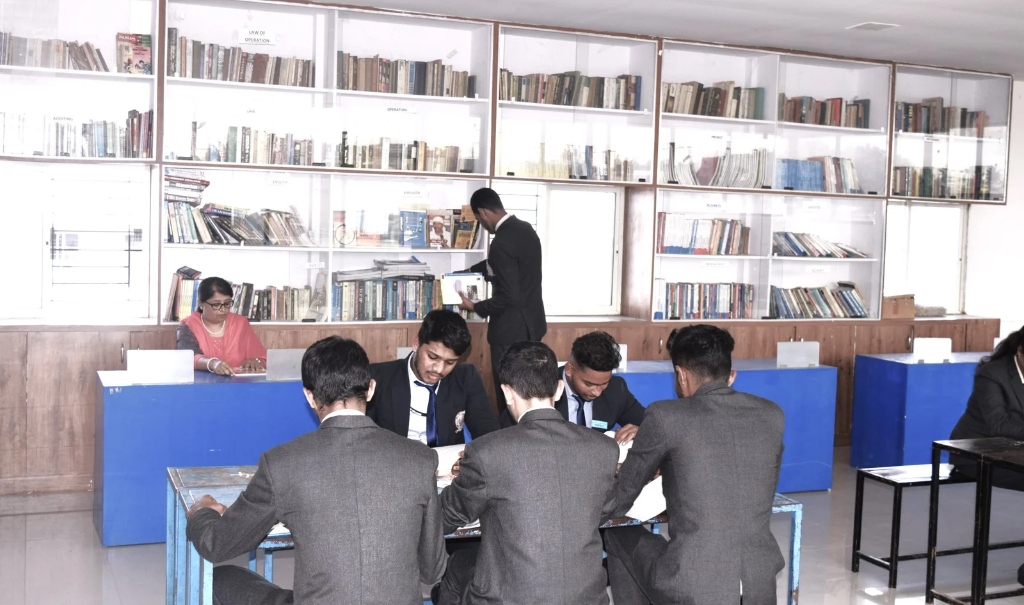A male student standing by a bookshelf reading a book in the library.